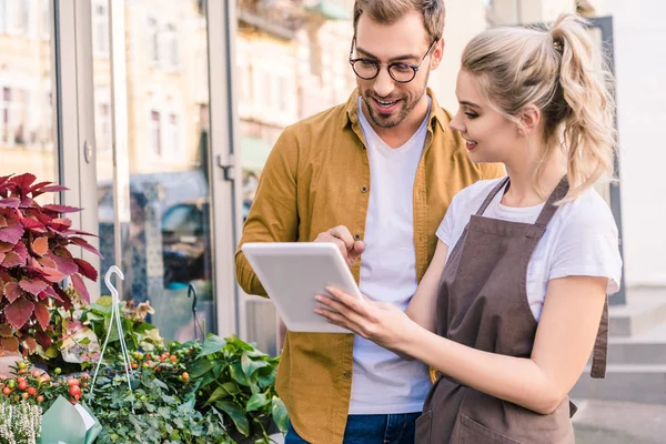 A florist with a new shop, shows a customer some of her available stock on an iPad.